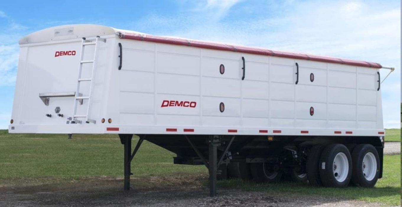 White Demco steel hopper-bottom grain trailer parked on level ground